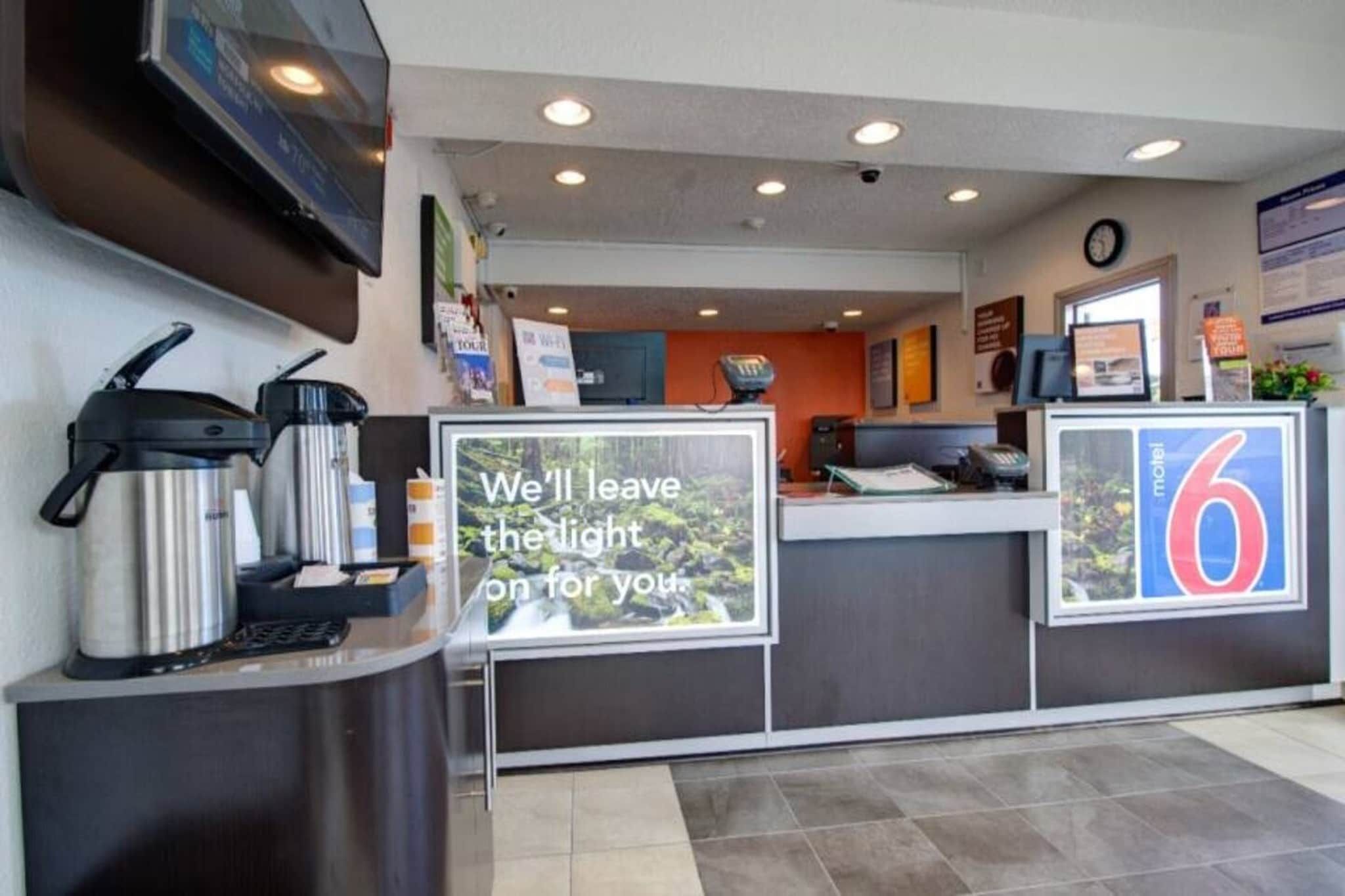 A hotel reception area with a coffee machine, a sign stating 'We'll leave the light on for you,' and a number '6' indicating the room number.