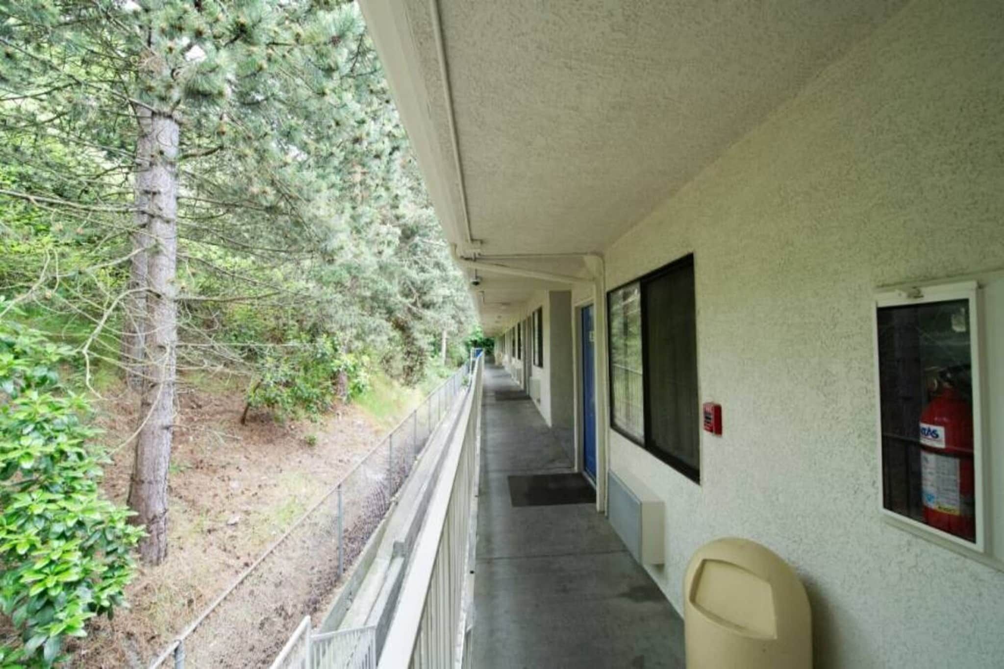 A corridor with a covered walkway, trees, and a fire extinguisher on the wall.