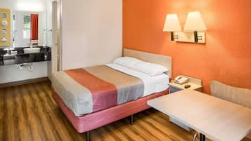 A hotel room with a bed, bedside table, and a small table with a chair.