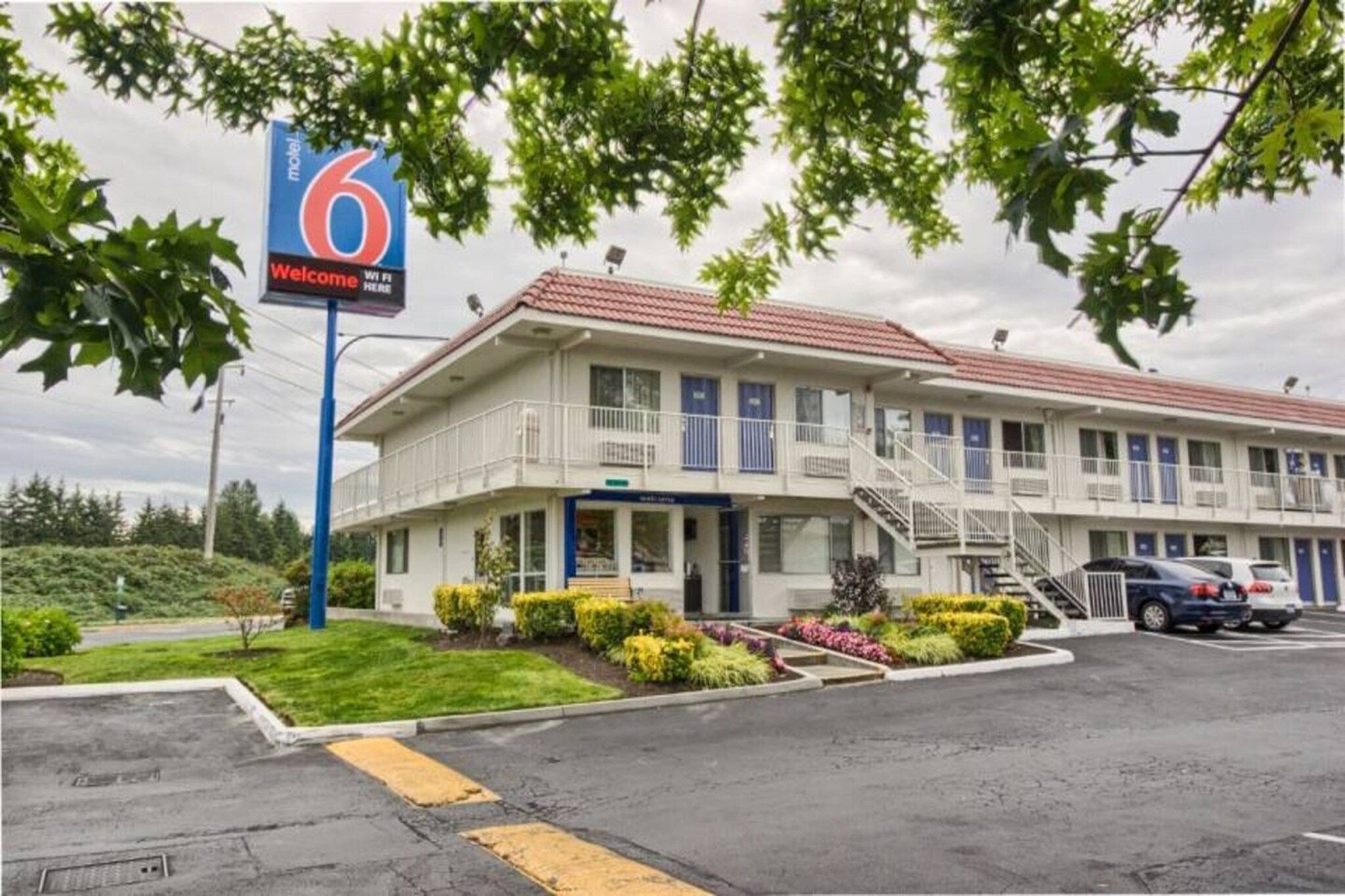 A motel with a sign indicating the number 6, a covered front porch, and a parking lot with cars.
