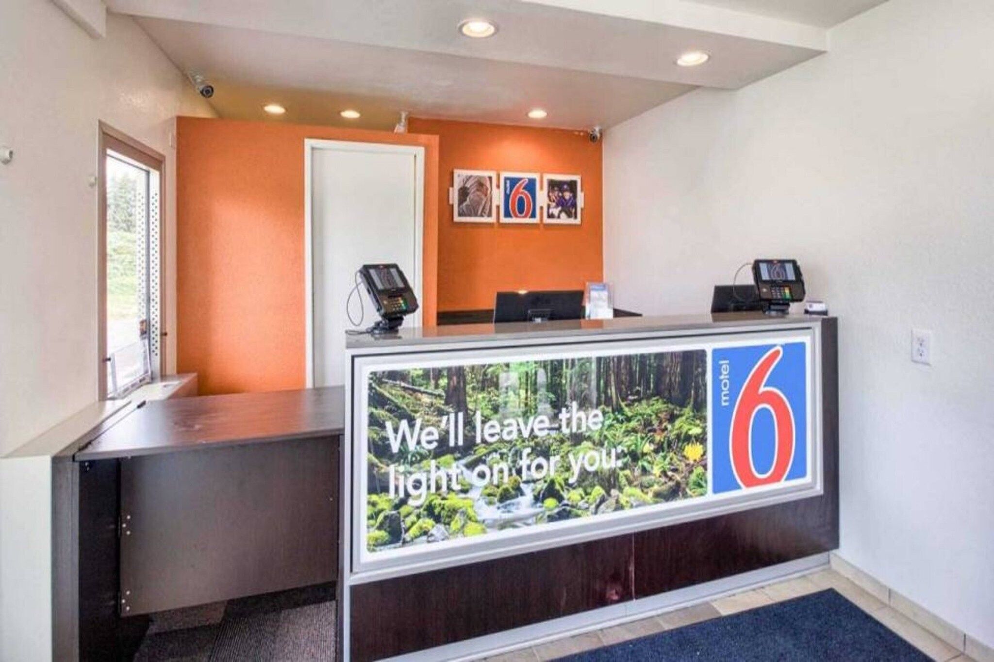 A hotel reception desk with a large window displaying a forest view, a digital screen, and a sign indicating room number 6.