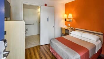 A hotel room with a bed, bedside table, lamp, and a door leading to a bathroom.