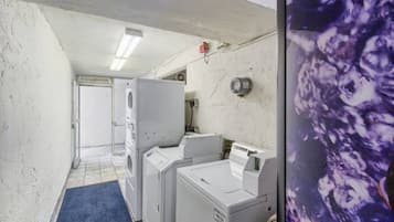 A laundry room with stacked washers and dryers, a blue mat on the floor, and a wall-mounted heater.
