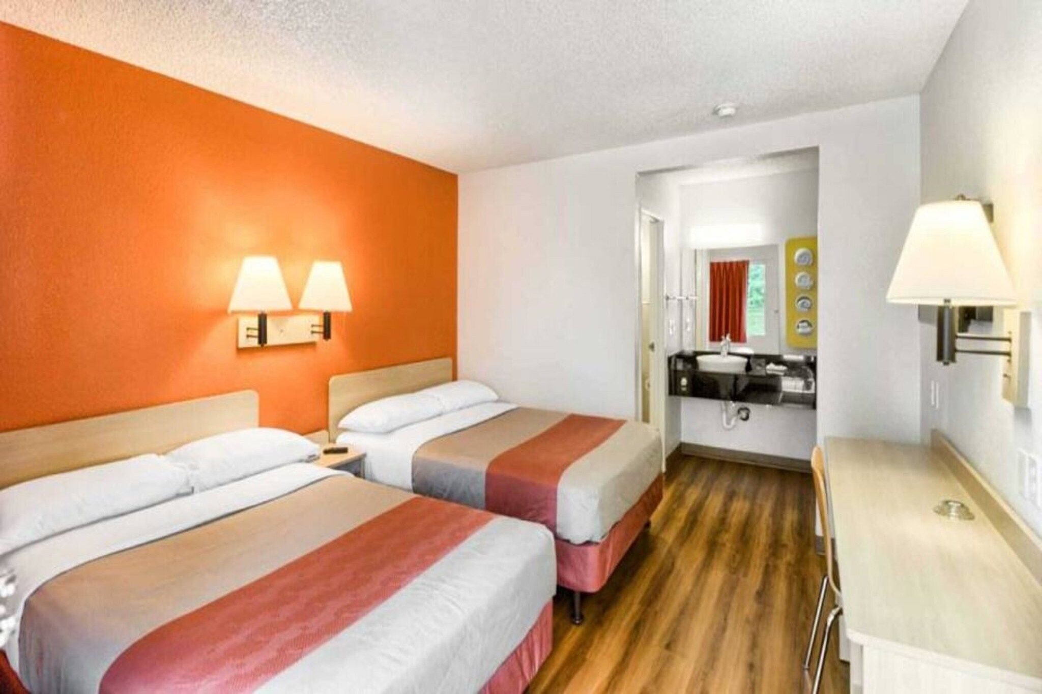 A hotel room with two beds, a desk, and a bathroom visible through an open door.