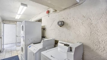 A laundry room with two stacked washers and dryers, a wall-mounted thermostat, and a door leading to another room.