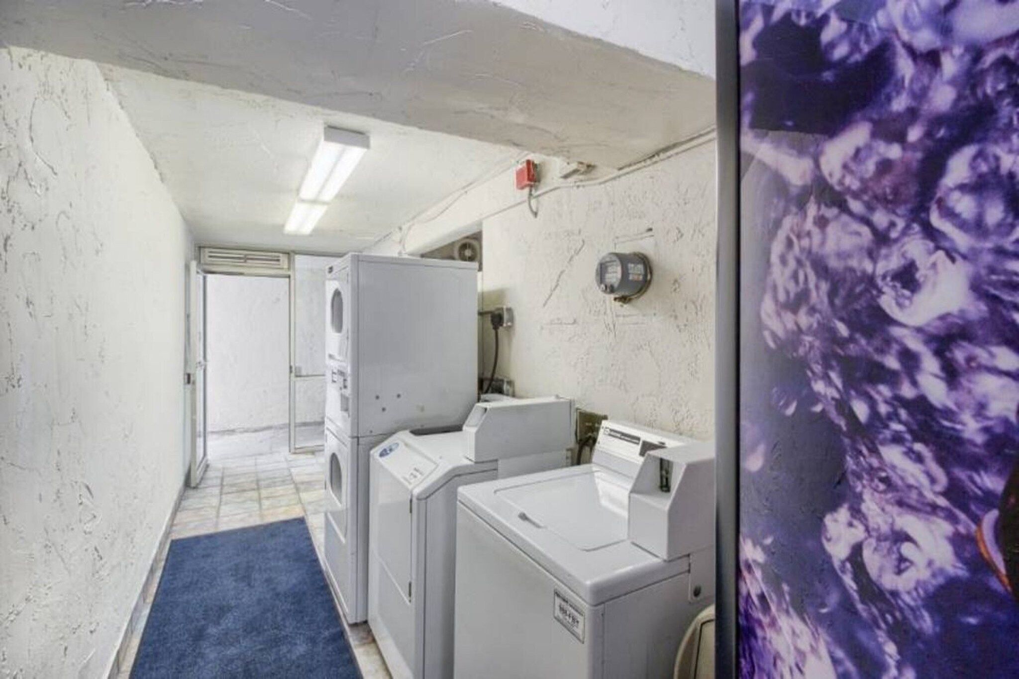 A laundry room with stacked washers and dryers, a blue mat on the floor, and a wall-mounted heater.