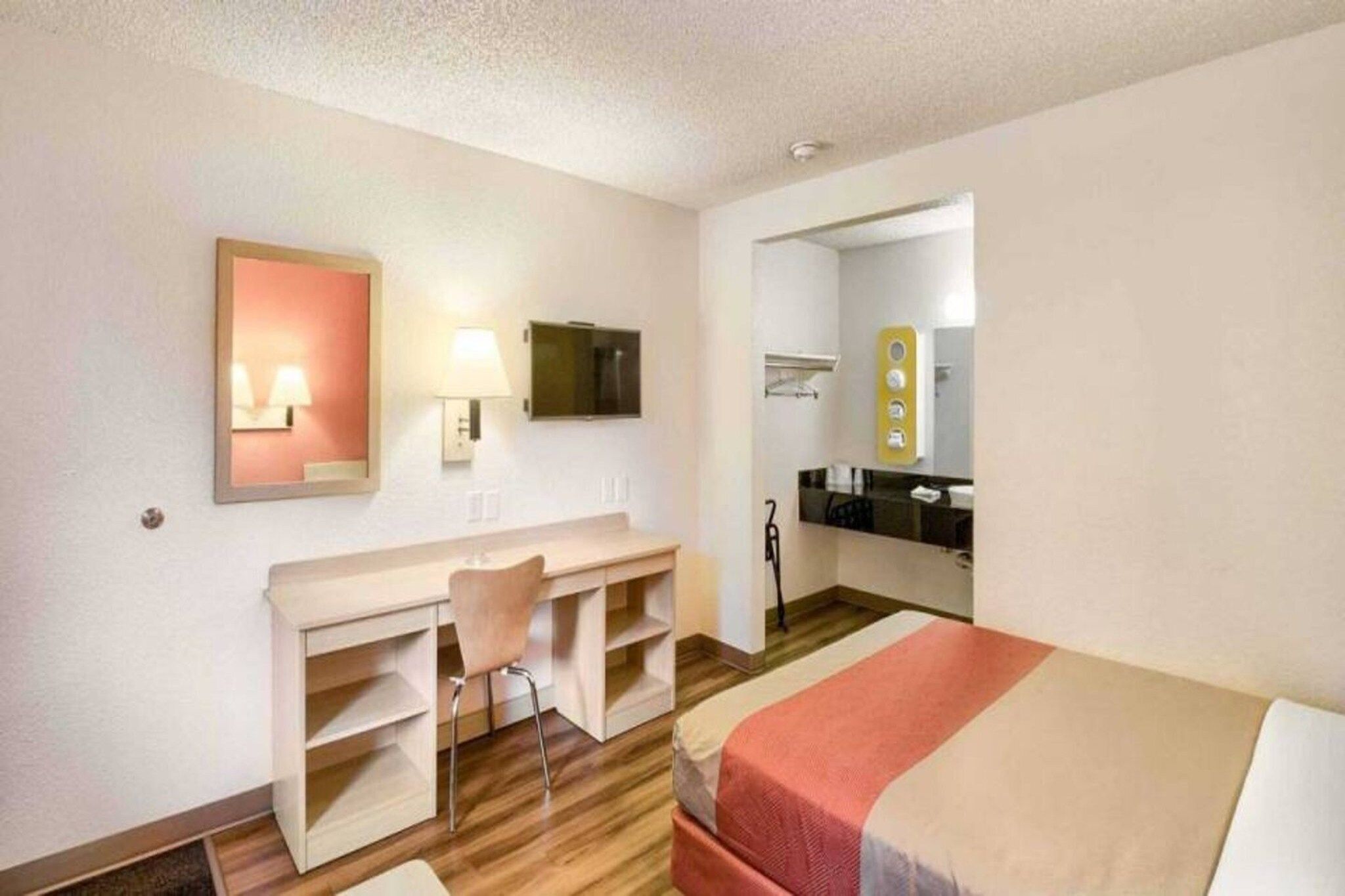 A hotel room with a bed, a desk, a chair, a mirror, and a bathroom visible through an open door.