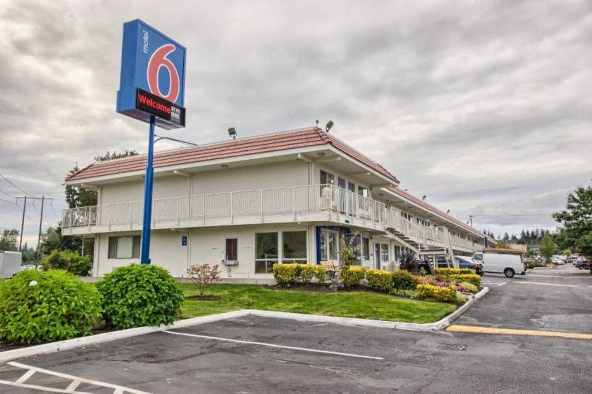 A motel with a large sign, a parking lot, and a building with a red roof.