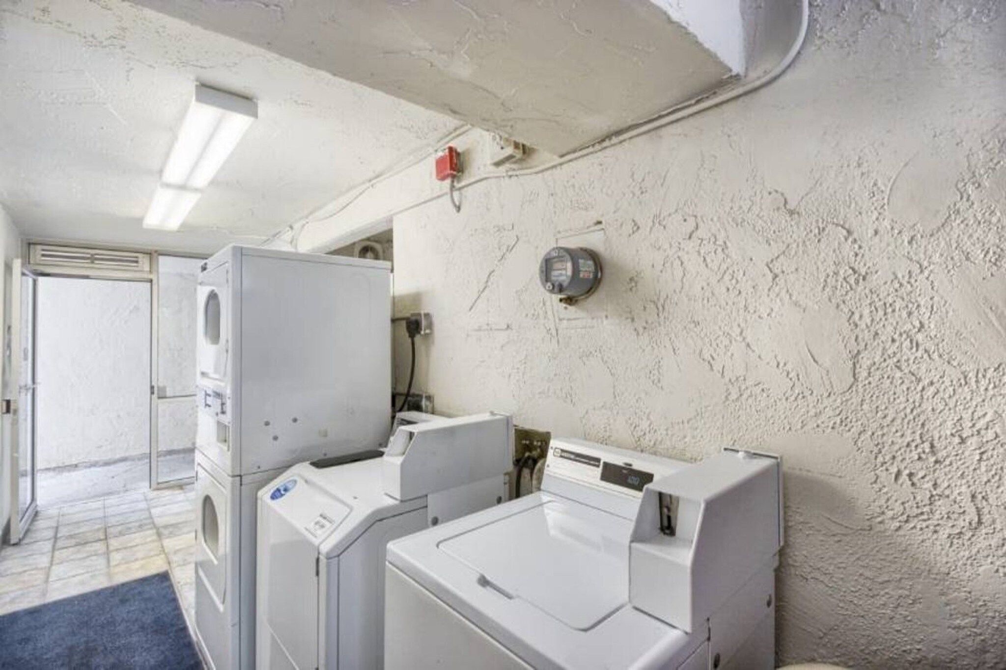 A laundry room with stacked washers and dryers, a water heater, and a door leading to another room.