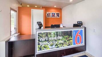 A hotel reception desk with a large window displaying a forest view, a digital screen, and a sign indicating room number 6.