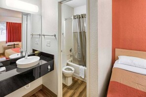 Hotellihuone, jossa on sänky, kylpyhuone, jossa on suihku, pesuallas ja wc.