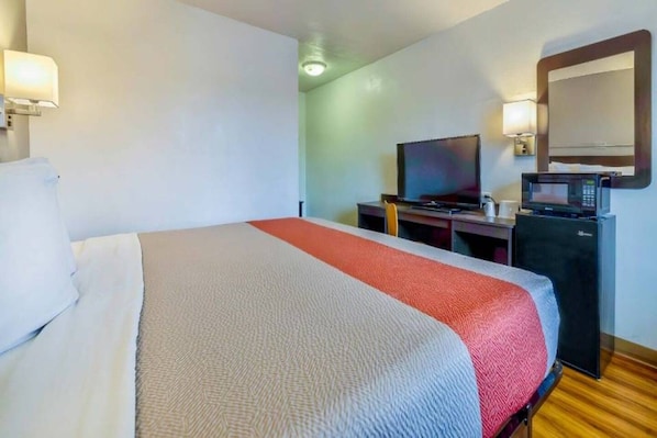 A hotel room with a bed, a desk with a television, a microwave, and a mirror.