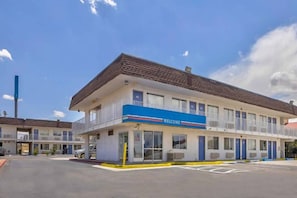 A motel with a blue 'WELCOME' sign, a covered parking area, and a clear sky.