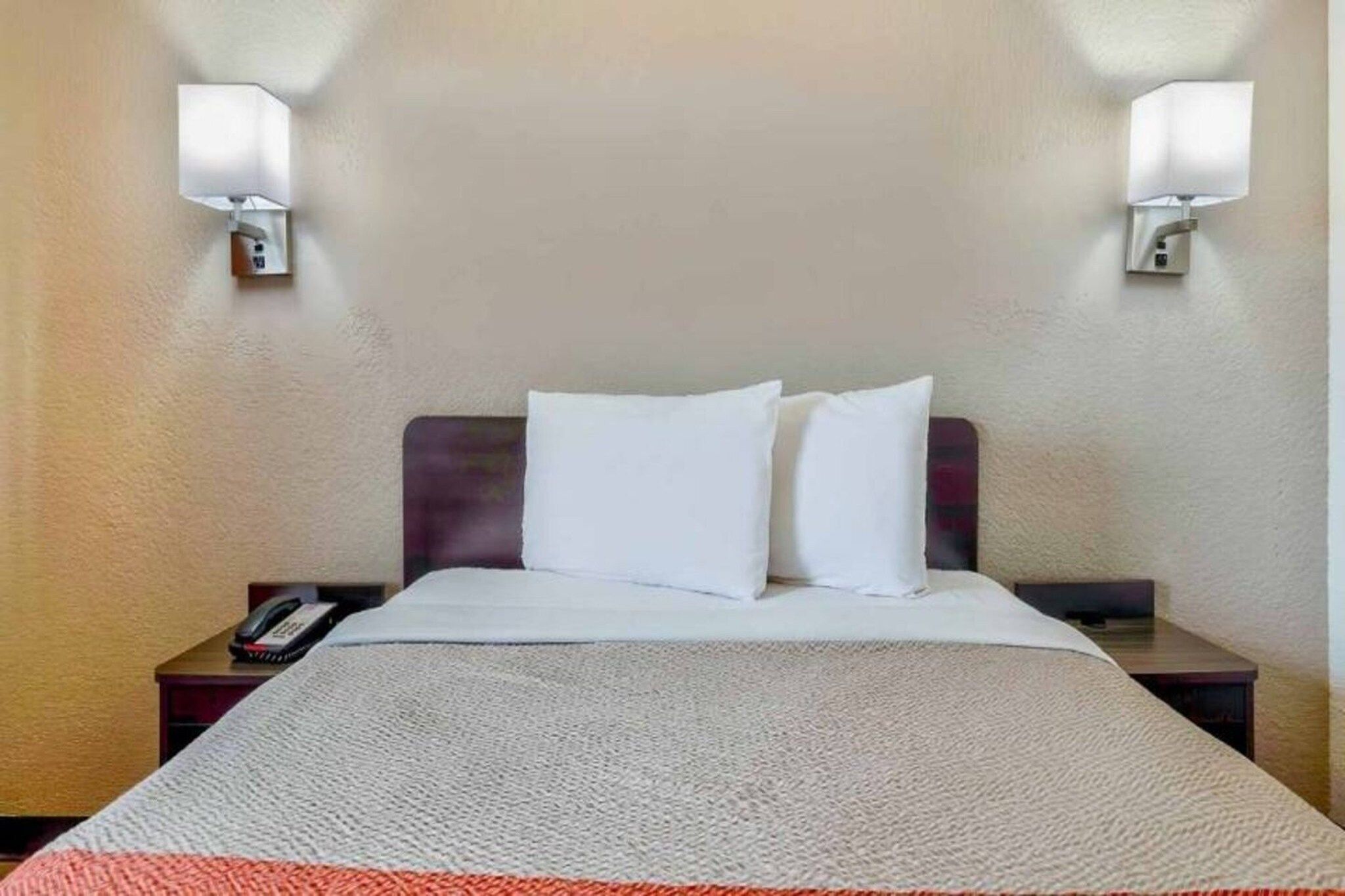 A hotel room with a bed, two bedside lamps, a telephone, and a carpeted floor.