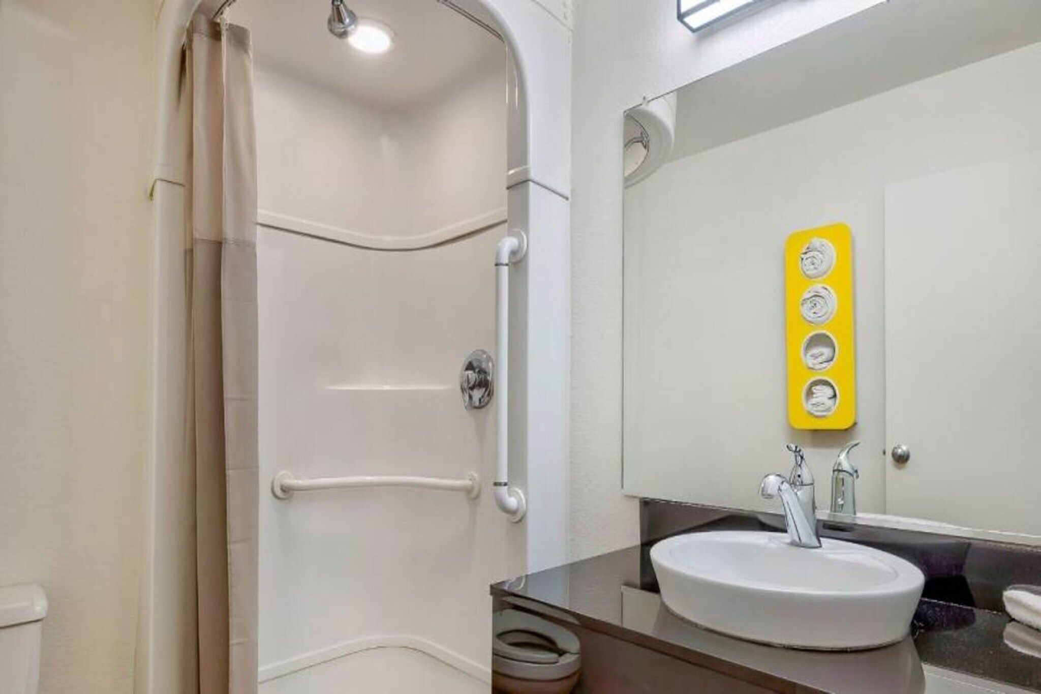 A modern bathroom with a walk-in shower, a sink with a mirror, and a yellow soap dispenser.