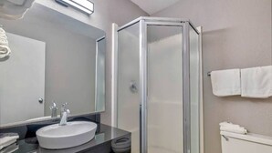 A bathroom with a glass-enclosed shower, a sink with a mirror above it, and a toilet. - MS6 Santa Rosa NM 1 Queen Bed | Non-Smoking (Santa Rosa NM)