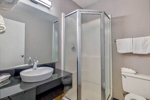 A bathroom with a glass-enclosed shower, a sink with a mirror above it, and a toilet. - MS6 Santa Rosa NM 1 Queen Bed | Non-Smoking (Santa Rosa NM)