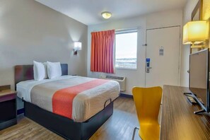 A hotel room with a bed, a desk, a chair, a window with curtains, a wall-mounted lamp, and a door. - MS6 Santa Rosa NM 1 Queen Bed | Non-Smoking (Santa Rosa NM)