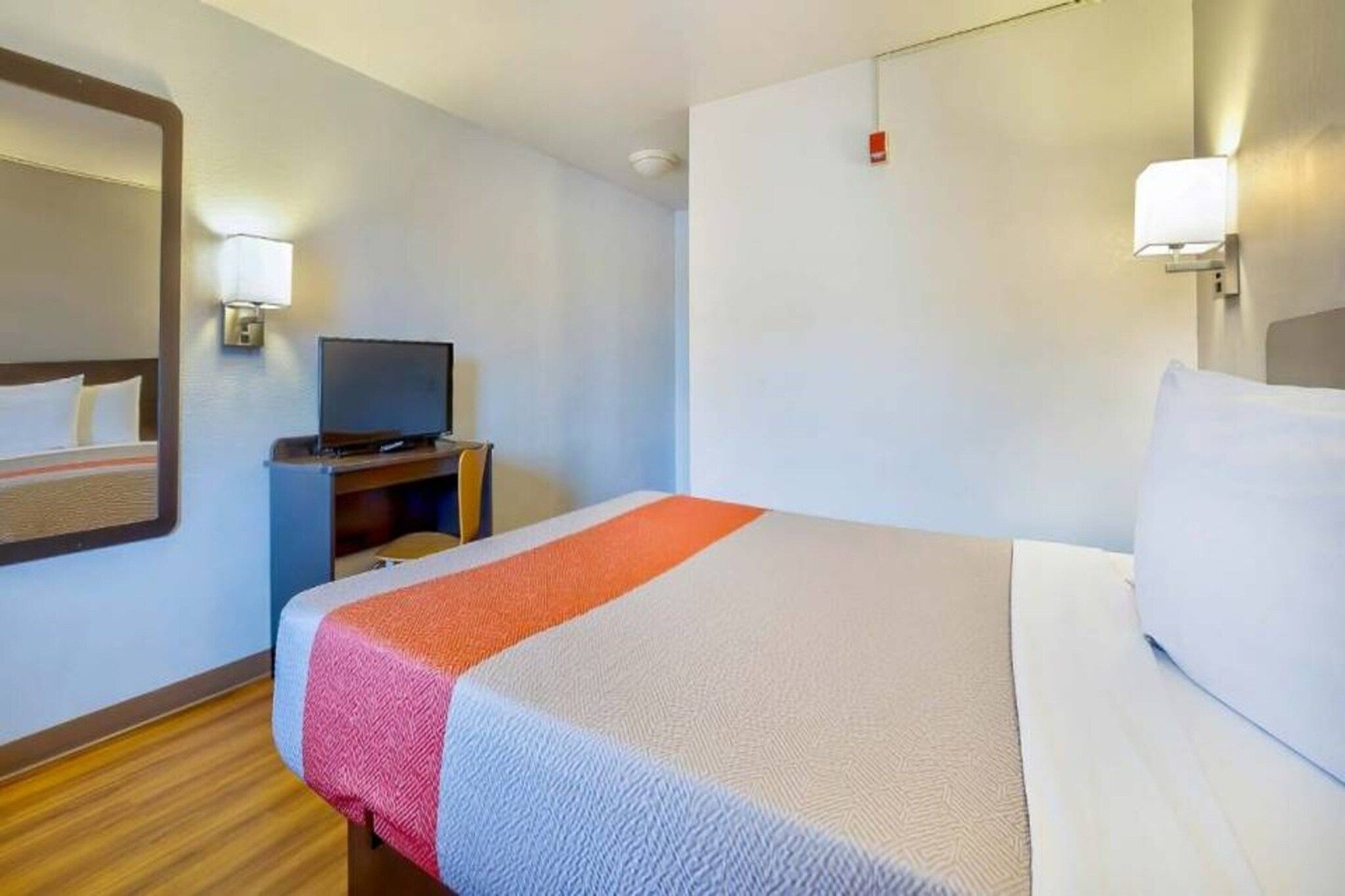 A hotel room with a bed, a television on a stand, and a nightstand.