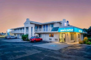 Ein Motel mit einem 'Welcome'-Schild, einem Parkplatz und zwei geparkten Autos davor.