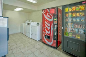 Una habitación con máquina expendedora, refrigerador y lavadoras apiladas.