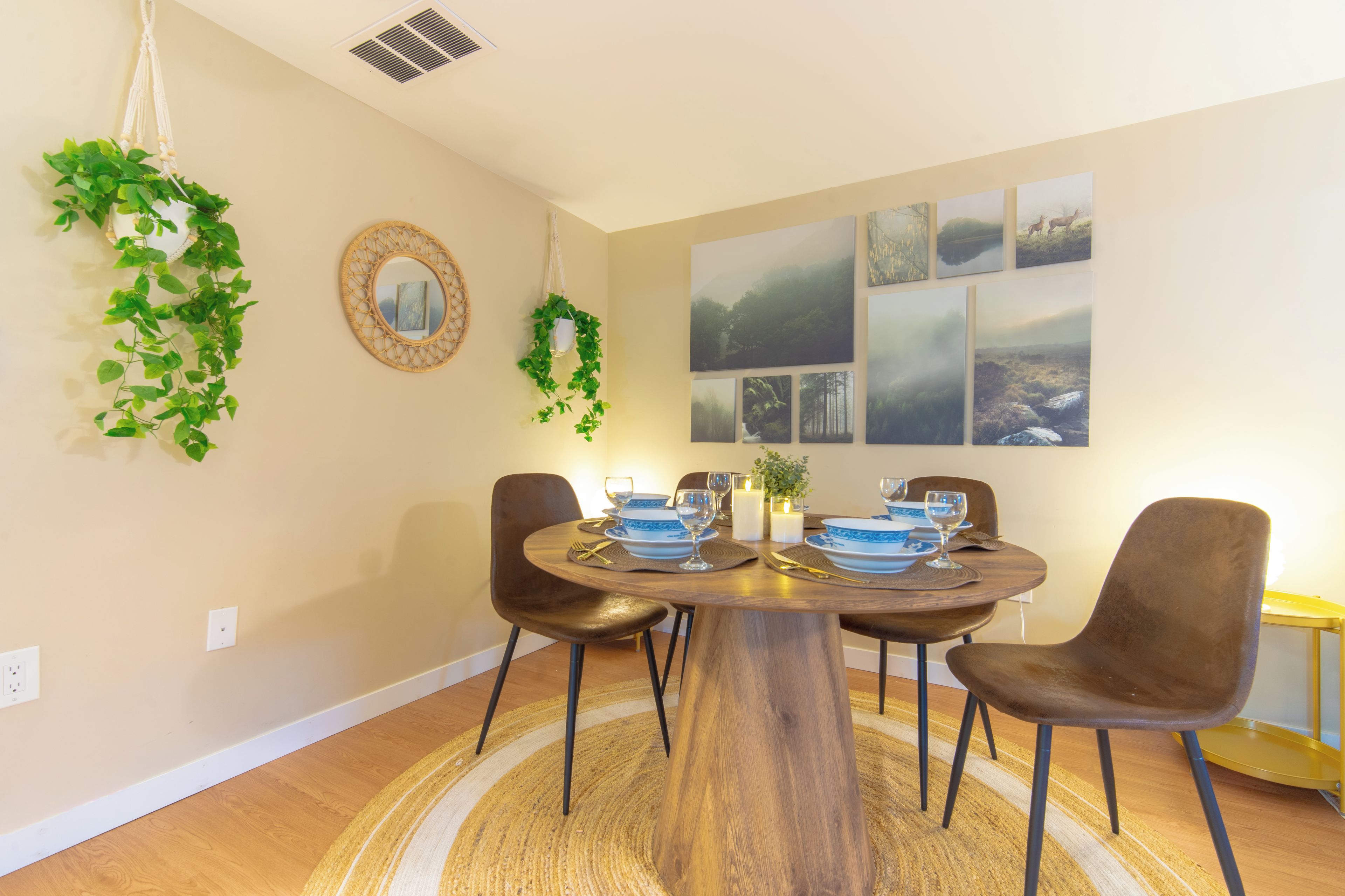 Un coin repas avec une table ronde, quatre chaises et une plante en macramé accrochée au mur.