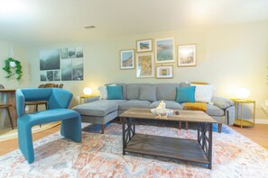Ein Wohnzimmer mit einer Eckcouch, einem blauen Sessel, einem Couchtisch und einem gemusterten Teppich.