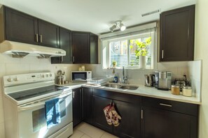 A modern kitchen with dark cabinetry, a white stove, and a window with a view of greenery. - Warm Modern Stay | 10 mins to Airport & Downtown (Calgary)
