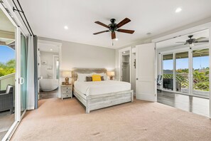 Ein Schlafzimmer mit einem Bett, Nachttischlampen, einem Deckenventilator und Blick durch eine offene Tür.