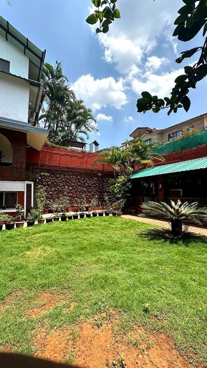 A courtyard with a grassy area, a stone wall, and a building with a red roof.