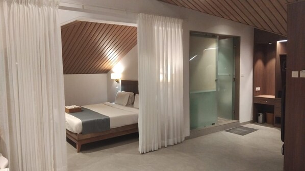 A modern bedroom with a bed, a bedside table, a glass shower enclosure, and a wooden ceiling.