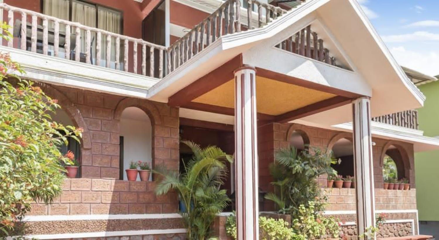A two-story building with a balcony, potted plants, and a stone facade.