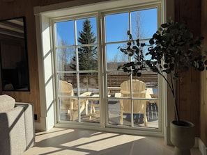 Une pièce dotée d’une grande porte-fenêtre coulissante donnant sur un patio extérieur aménagé avec des meubles en bois et un pot de fleurs.