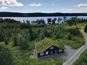 A house with a grass roof surrounded by dense forest, near a lake with a clear sky.