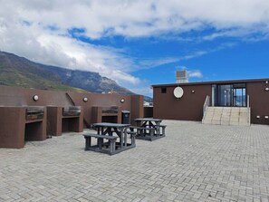 Ein Außenbereich mit einer Terrasse, Backsteinpflasterung, Tischen und Blick auf Berge.