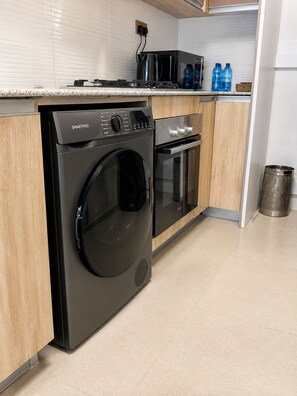 Eine moderne Küche mit einer Frontlader-Waschmaschine, einem eingebauten Backofen und einer Mikrowelle.