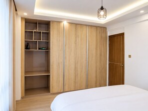 A bedroom with a large wardrobe, a bed, and a hanging light fixture. - 1 Bedroom in Westlands | Pool & Gym (Nairobi)