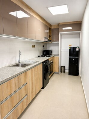 Une cuisine moderne avec des meubles en bois, un évier en acier inoxydable, un réfrigérateur noir et un four à micro-ondes.