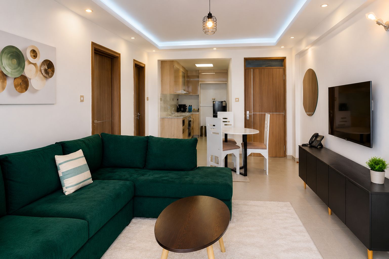 Uma sala de estar moderna com um sofá seccional verde, uma mesa de centro redonda e uma TV fixada na parede.