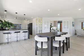 A modern kitchen with a dining area, featuring a central island, bar stools, and a table with chairs. - Summer Breeze Staycation (Tasman City)