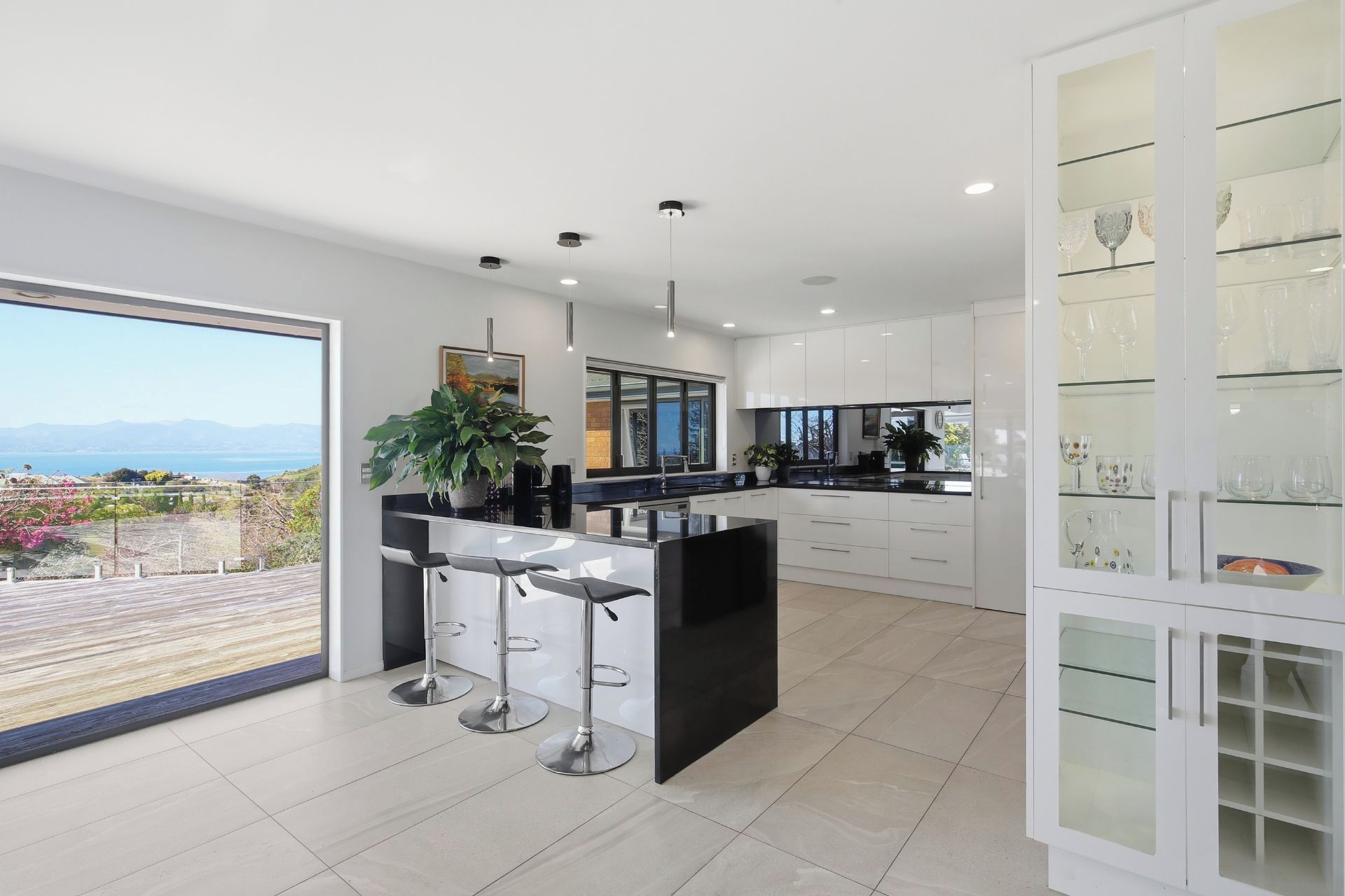 A modern kitchen with a large island, bar stools, and a glass cabinet with kitchenware.