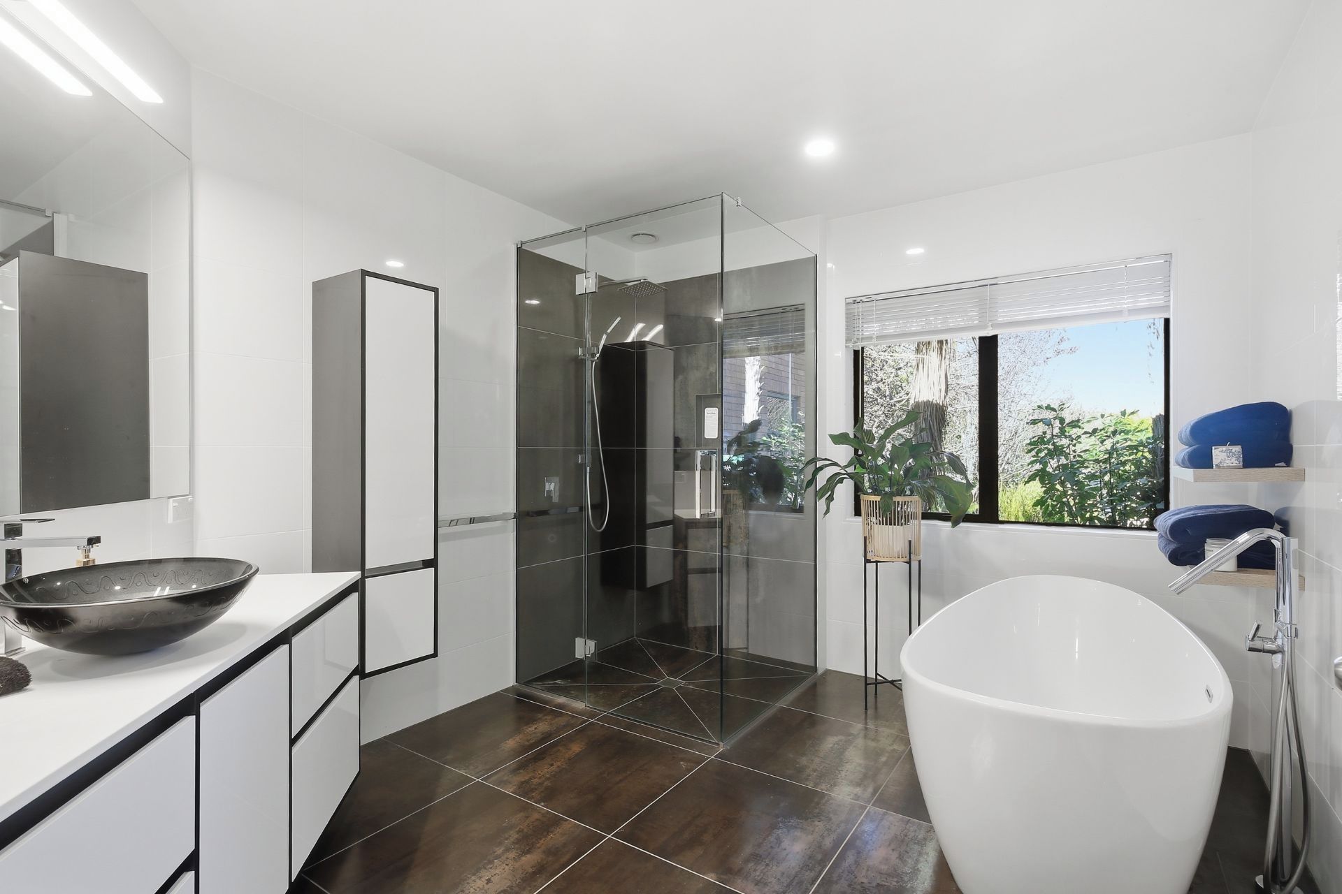 Een moderne badkamer met een groot, wit bad, een douche met glazen wanden en een grote spiegel.