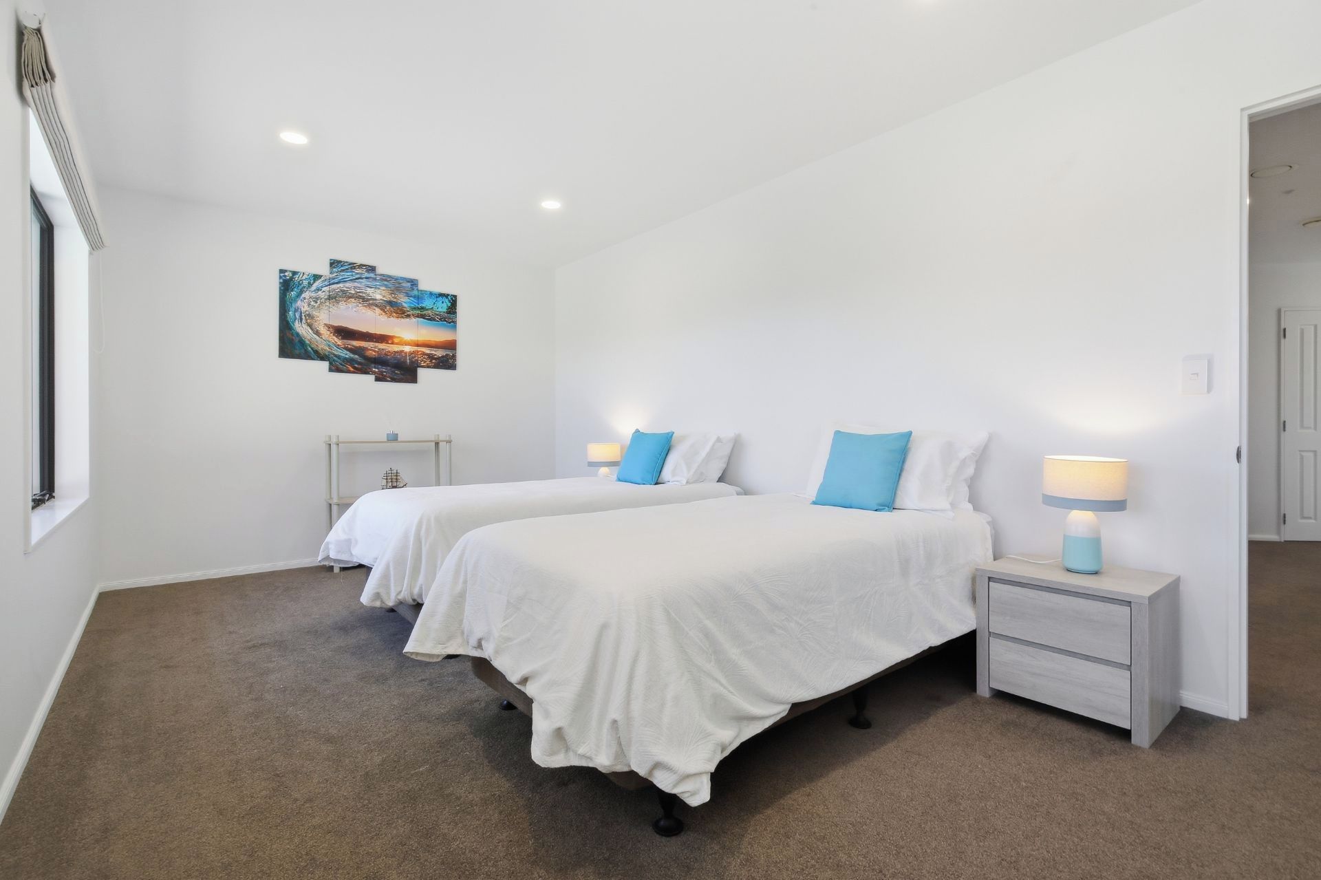A hotel room with two beds, a nightstand with a lamp, a painting on the wall, and a carpeted floor.