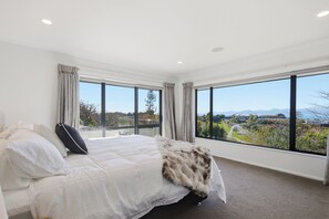 A bedroom with a large bed, two windows, and a view of a landscape. - Summer Breeze Staycation (Tasman City)