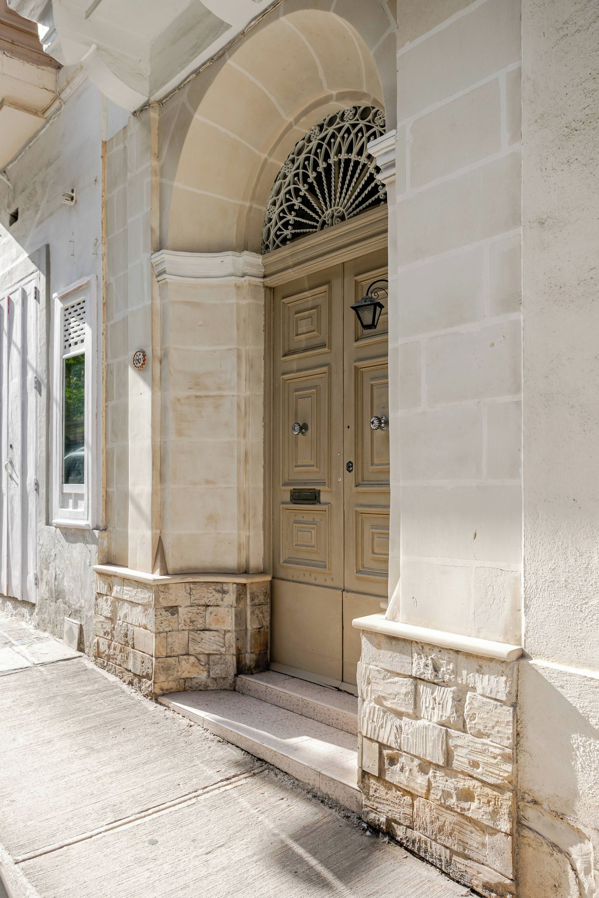 A building facade with a large arched entrance, stone steps, and a door with a decorative fanlight above.