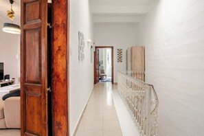 Un couloir avec une porte en bois, un mur blanc, un sol carrelé et une rambarde en métal.