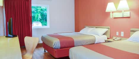 Habitación de hotel con dos camas, un escritorio, una silla, un televisor y una ventana con vistas a zonas verdes.