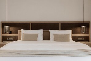A neatly made bed with a wooden headboard, two bedside tables with lamps, and a textured wall panel. - Enigma Mykonos Hideaway Suites (Mykonos)