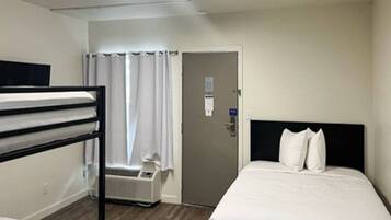 A hotel room with a bunk bed, a single bed, a door with a window, and a wall-mounted air conditioning unit.