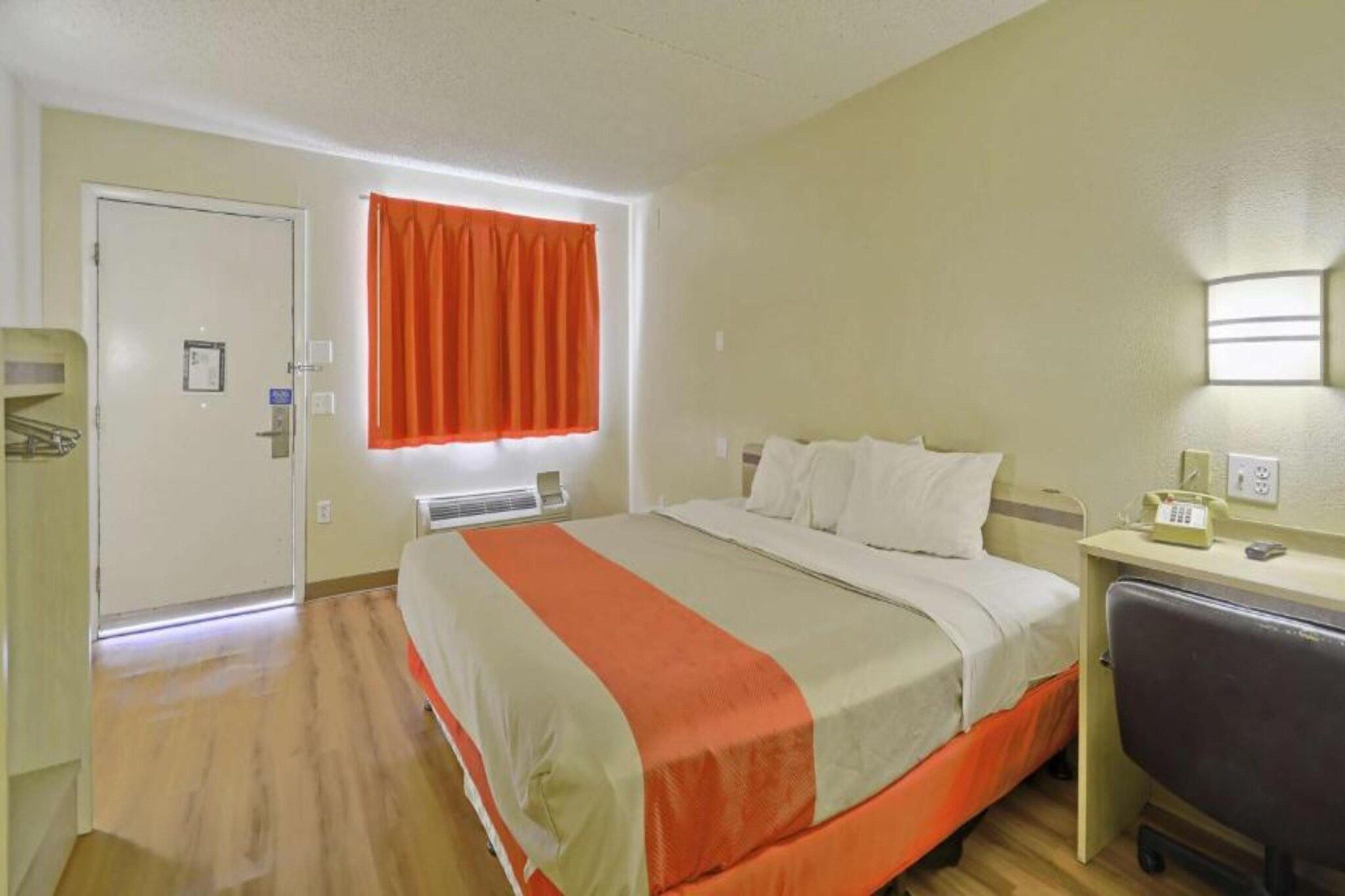 Une chambre d’hôtel avec un lit, un bureau, une chaise, une fenêtre avec des rideaux et une porte.